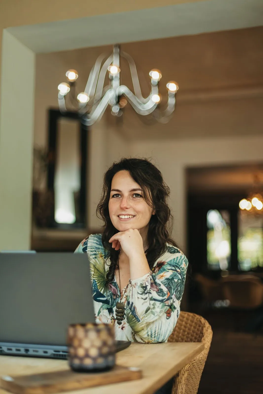 Simone lacht met haar kin op haar hand, achter haar laptop